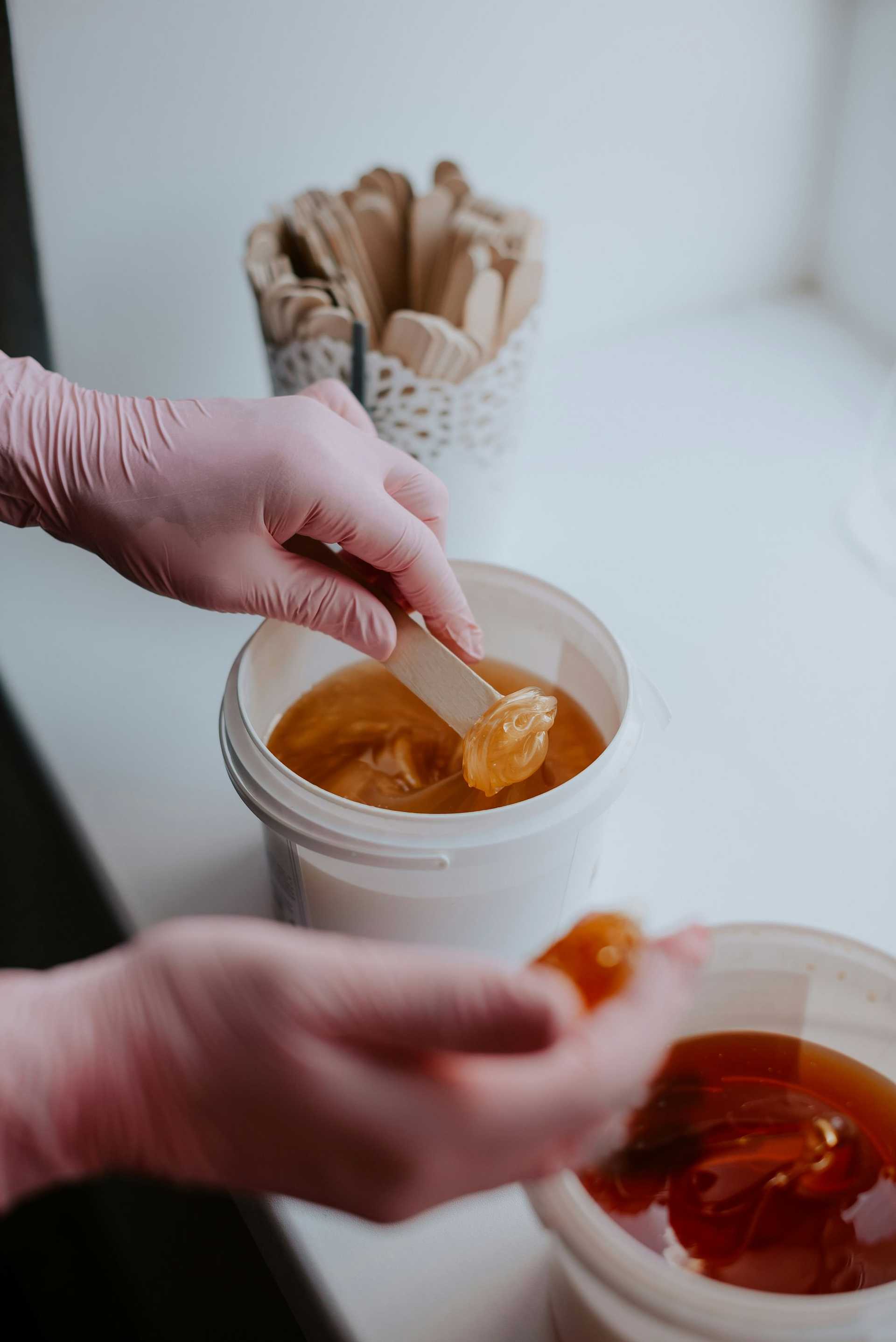 Hands with gloves preparing wax for hair removal.